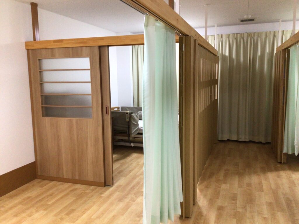 木製仕切りとカーテンで区切られた居室。複数ベッドスペースが見える。